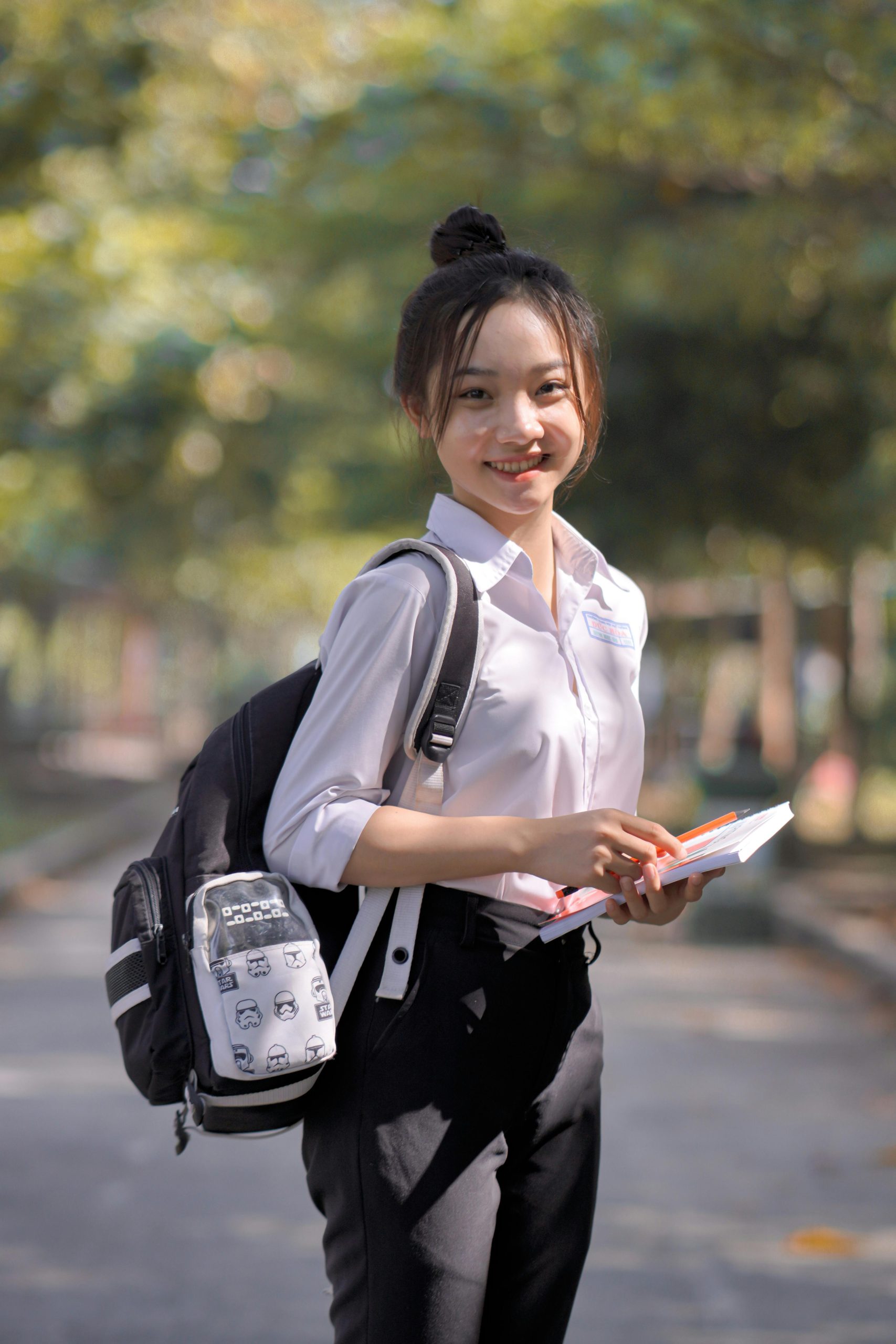Portrait of a cheerful student with a backpack and notebooks in a sunny park setting.